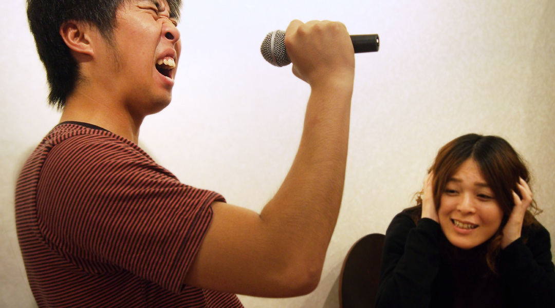 割れんばかりの大きな声で歌う男性と耳を塞ぐ女性